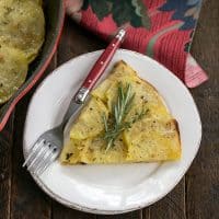 Overhead view of a slice of potato galette on a round white plate with a red handle fork