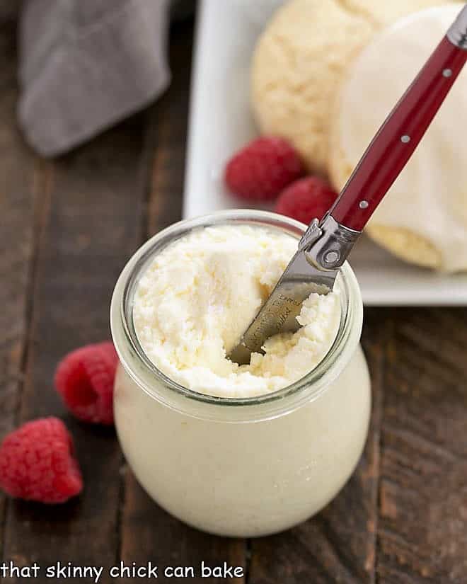 Overhead look into a Instant Pot Clotted Cream Recipe in a Weck jar with berries, scones and a red handled knife.