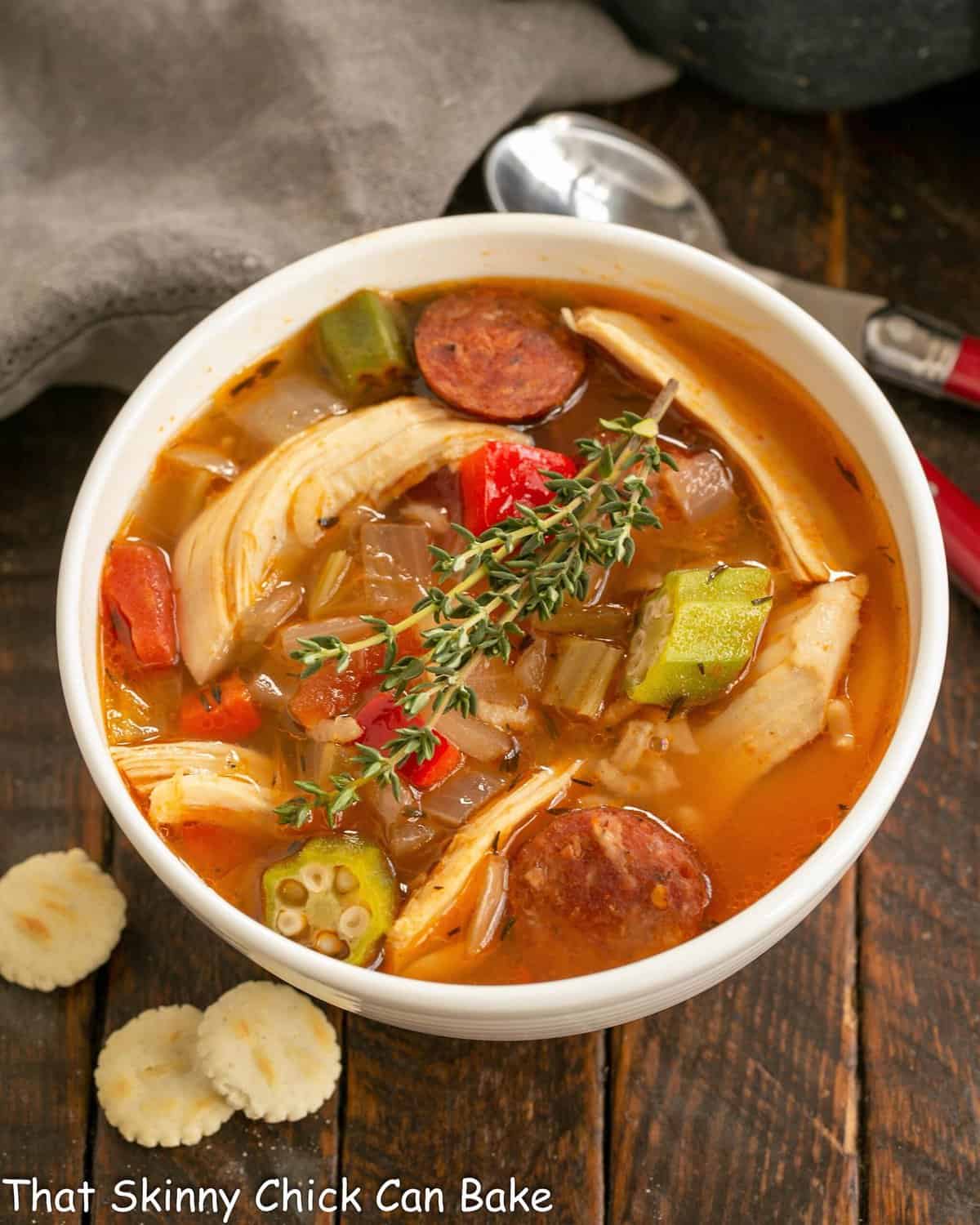 Overhead view of jambalaya soup in a white bowl with oyster crackers.