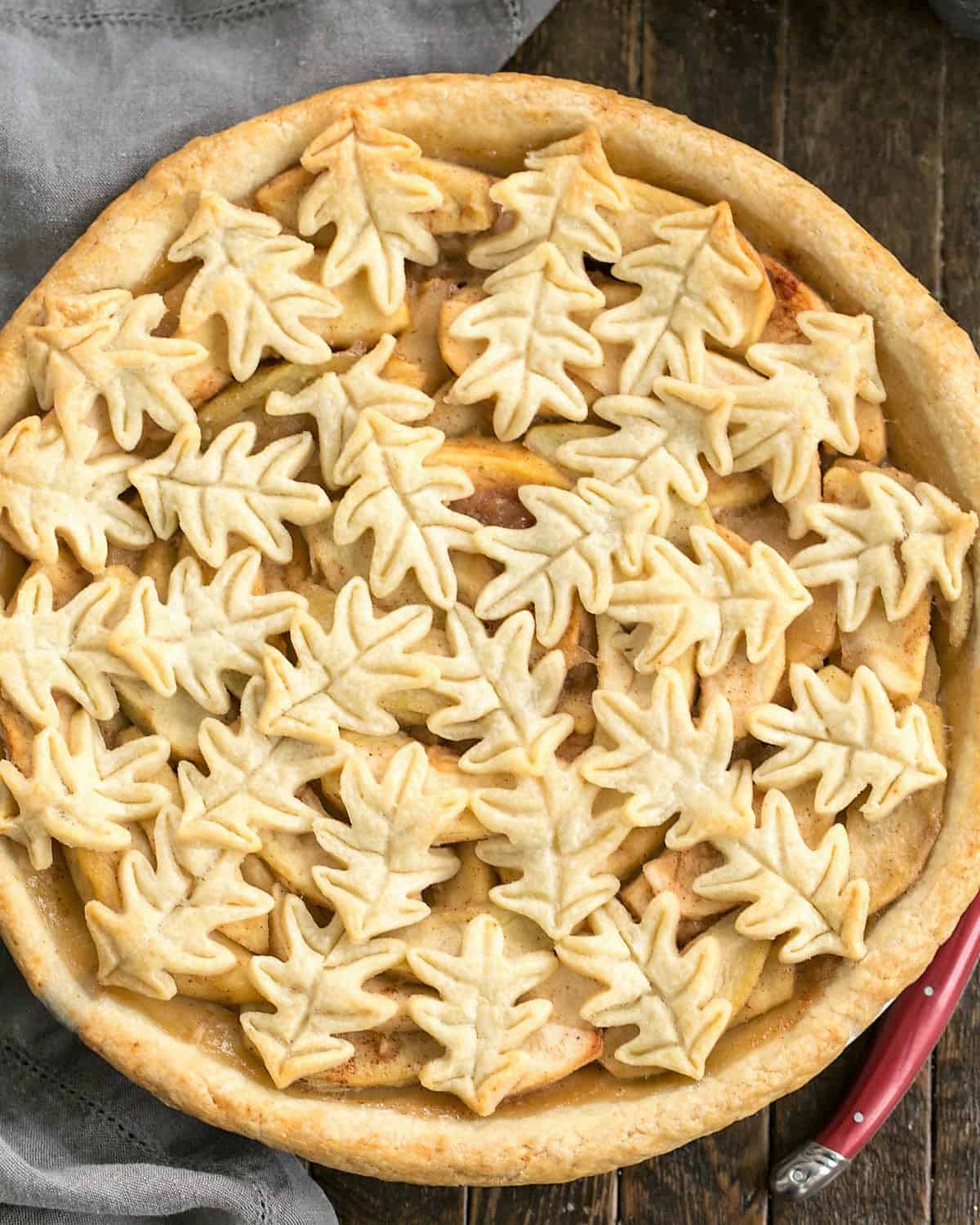 Overhead view of apple pie with a leaf topping with a red handle knife.