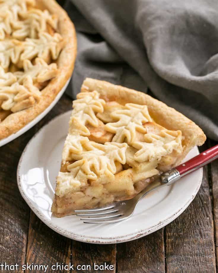 Slice of apple pie on a round white plate with a red handled fork