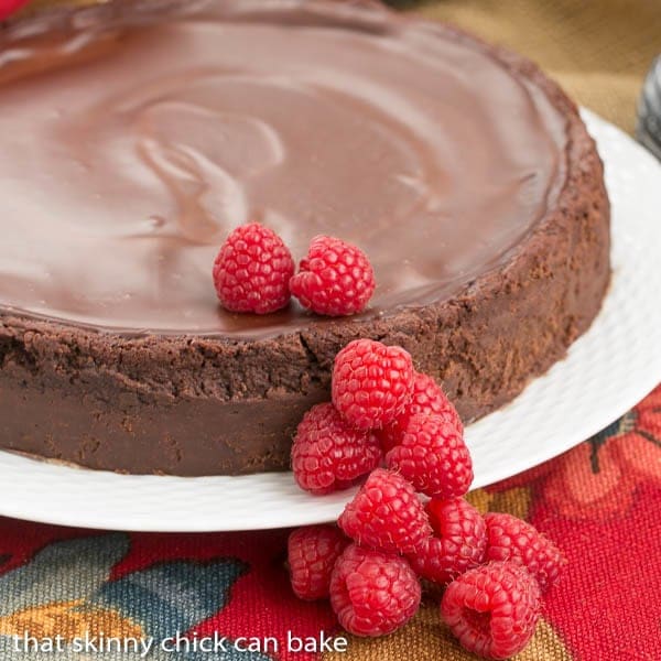 A cake platter holding flourless Chocolate Torte topped with chocolate ganache.