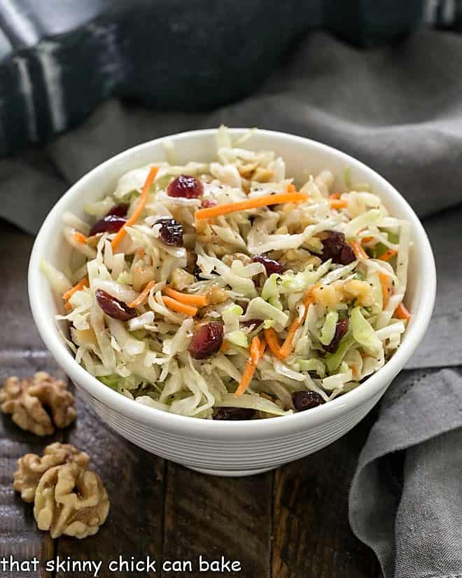 Easy coleslaw in a white bowl with walnuts to garnish.