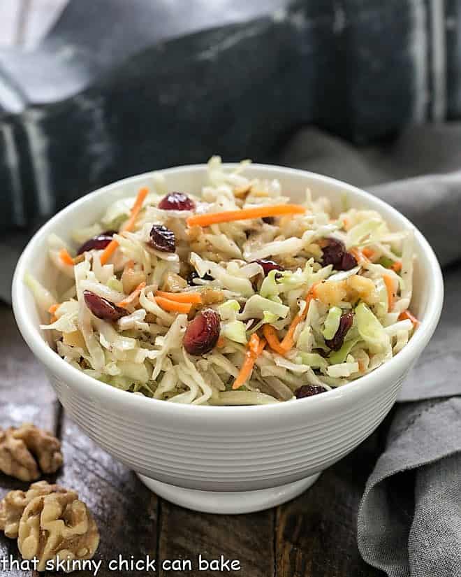 Easy coleslaw recipe in a small white ceramic bowl with a gray napkin and walnut halves.