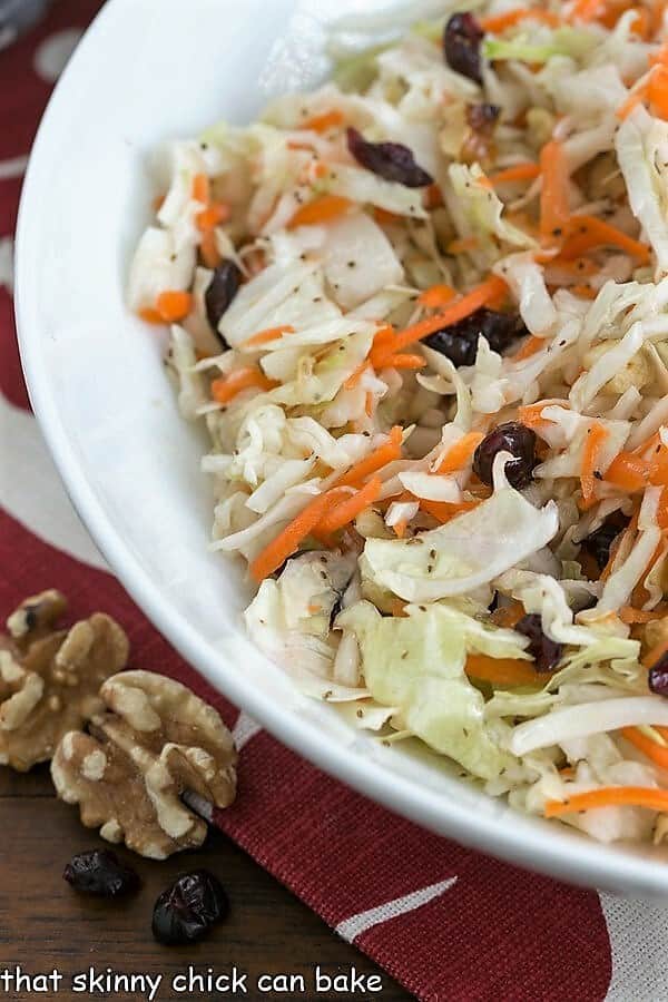 This easy coleslaw recipe can be put together in minutes. Dotted with vibrant dried cranberries and crunchy walnuts, it's a crowd pleasing side dish recipe. This coleslaw recipe without mayo is perfect for cookouts, picnics, and potluck dinners. Close view of a white bowl of homemade Coleslaw without mayo