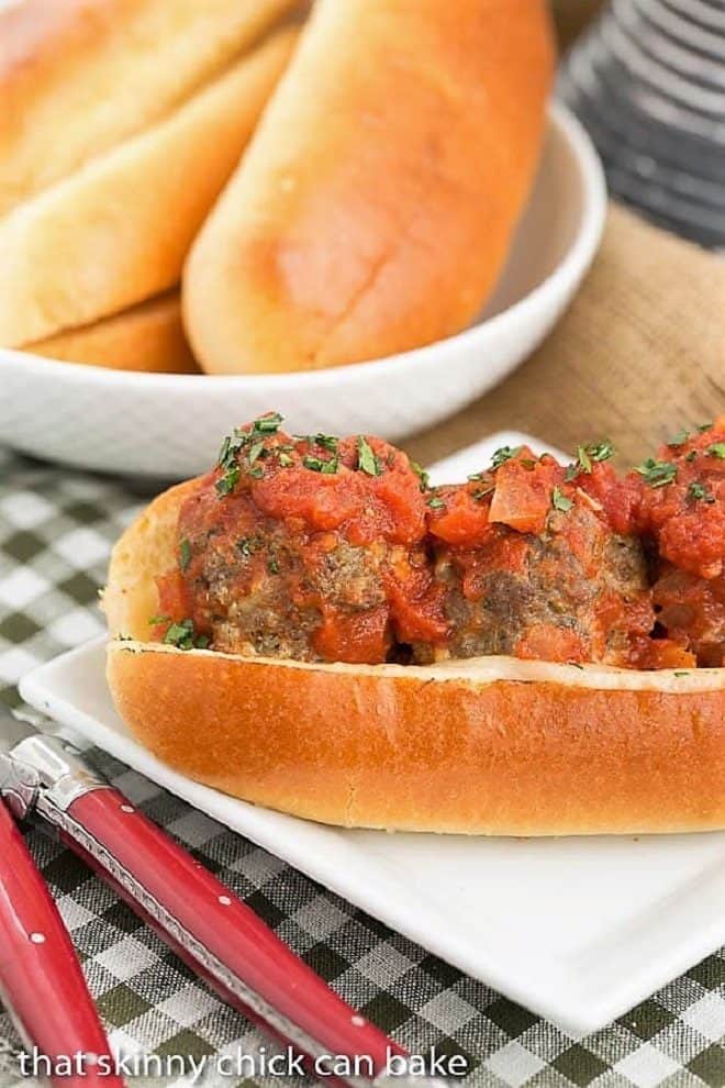 Meatball Subs on a white plate with a bowl of buns in the background