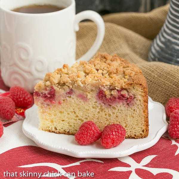 A piece of raspberry coffee cake on a white plate with two raspberries