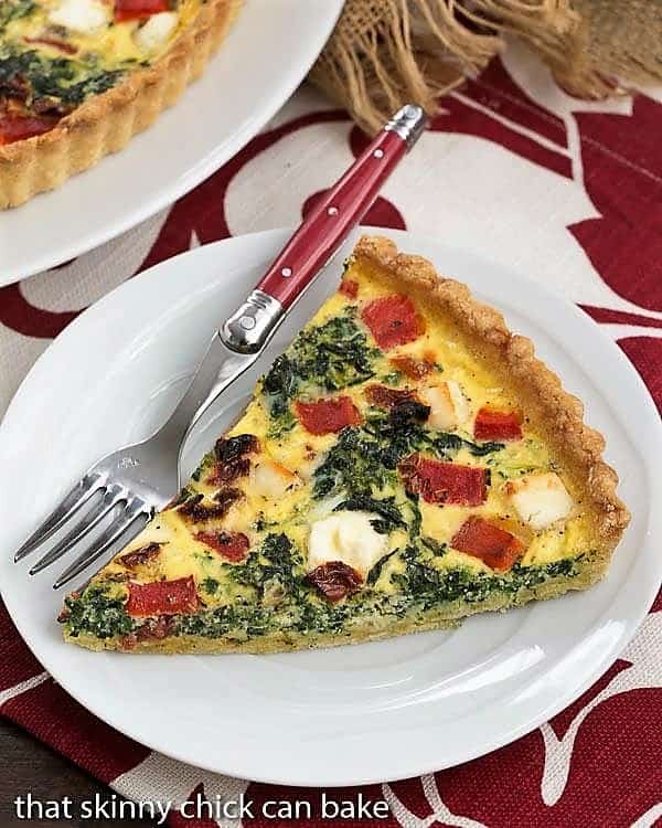 Sun-dried Tomato and Spinach Quiche slice on a white plate on a red and white napkin.