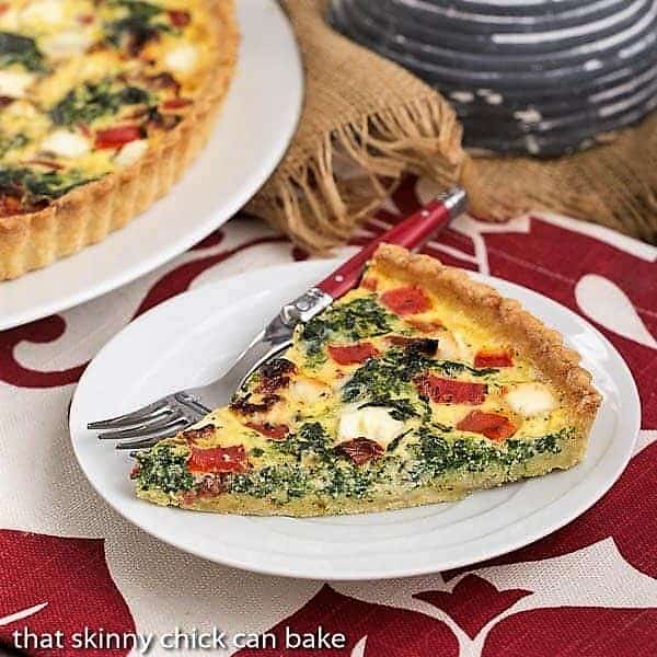 Sun-dried Tomato and Spinach Quiche slice on a white plate with a red handled fork.