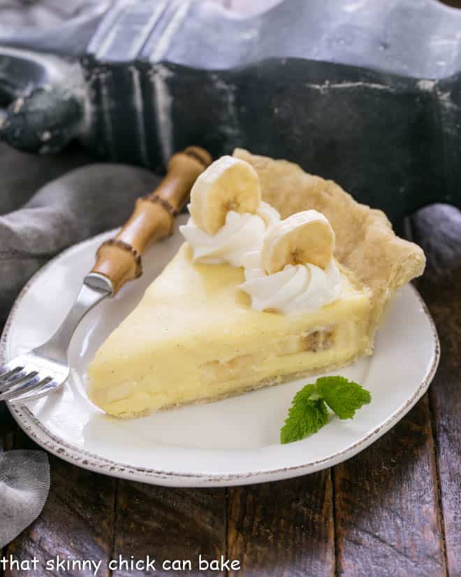 Slice of the best banana cream pie on a white plate with a sprig of mint