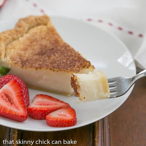 Sugar Cream Pie bite on a fork with pie slice and strawberries on a dessert plate in the background.