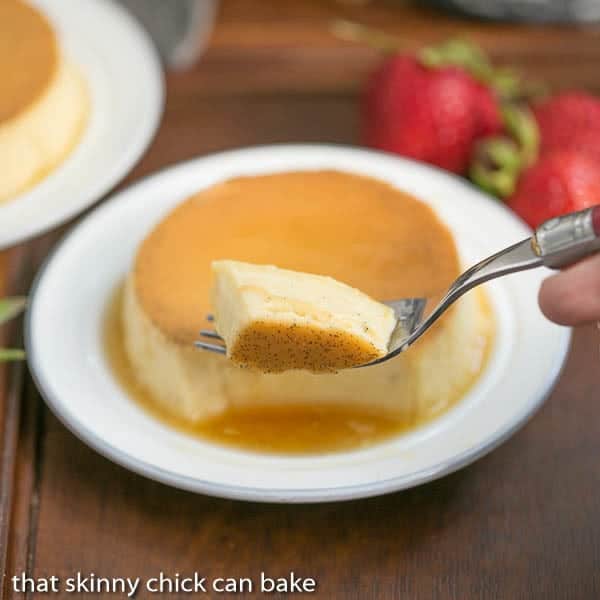 Forkful of mini vanilla flans with mini flan on a white plate in the background.