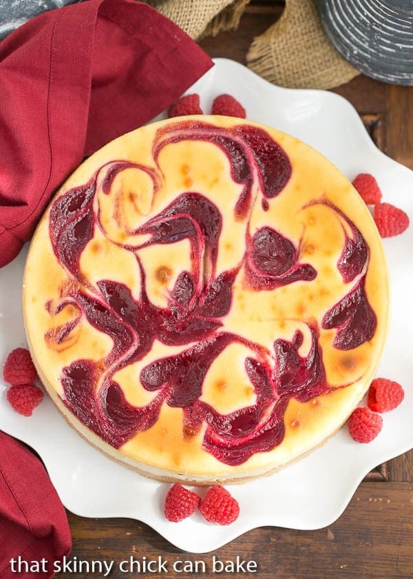 Overhead view of White Chocolate Raspberry Swirl Cheesecake on a white serving plate with fresh raspberries