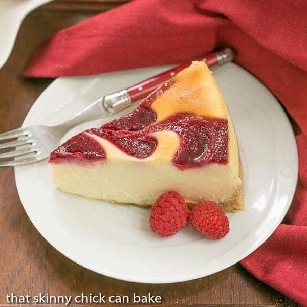 White Chocolate Raspberry Swirl Cheesecake slice on a white plate with fresh raspberries