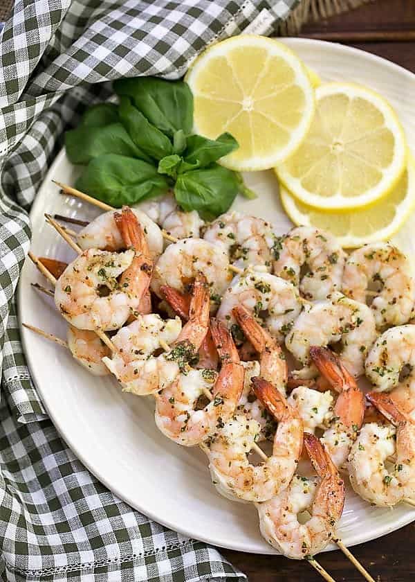 Grilled Shrimp Scampi on skewers on a serving plate with basil and lemon slices.