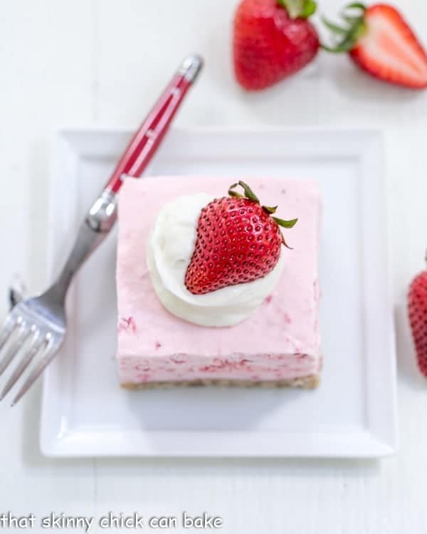 Вид сверху на кусочек клубничного десерта на квадратной белой тарелке с вилкой с красной ручкой.