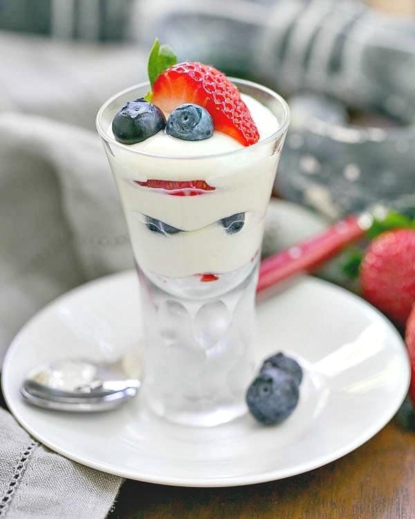 White Chocolate Berry Parfaits in a clear cordial glass on a white ceramic saucer