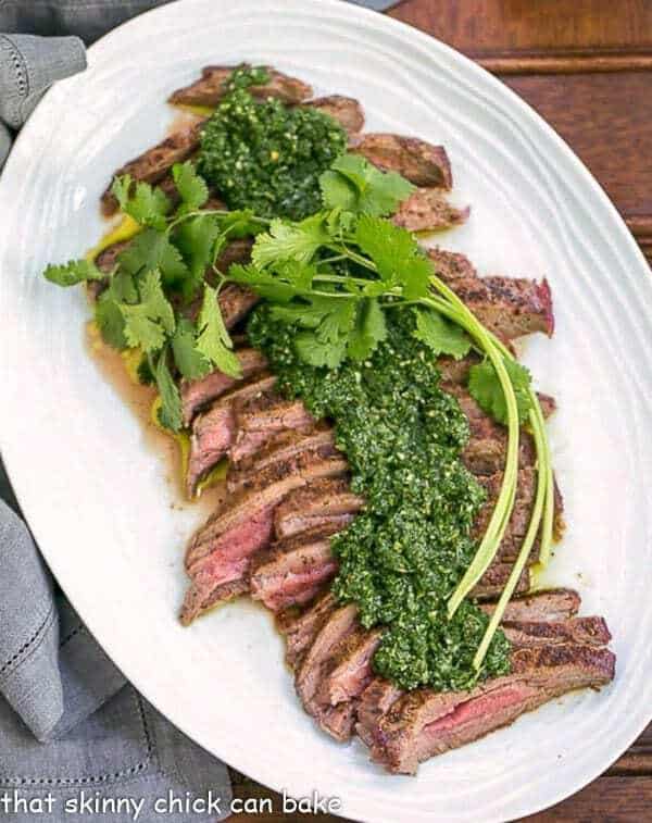 Overhead view of Grilled Flank Steak with Chimichurri Sauce on a white oval platter.