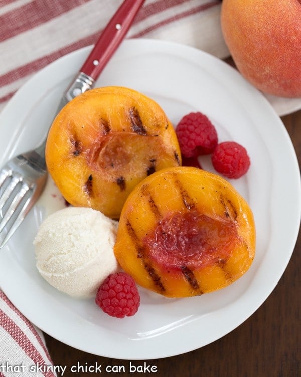 Overhead view of Grilled Peach Melba on a white plate with a fork and scoop of ice cream