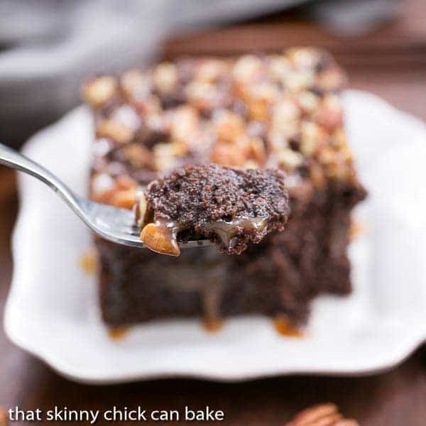 A slice of turtle poke cake with a forkful in the foreground