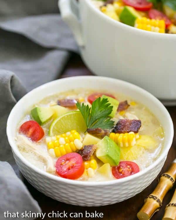 A white bowl filled with corn chowder with a large pot behind it.
