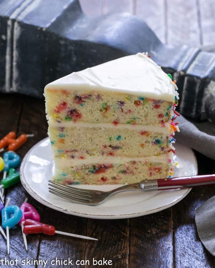 Slice of funfetti cake on a white dessert plate with a red handle fork