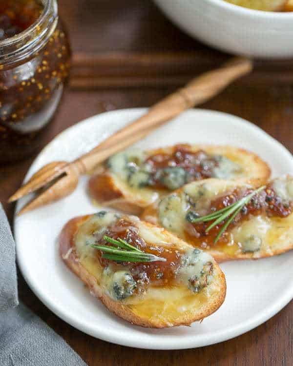 Fig Gruyere Crostini on a white appetizer plate with a wooden honey drizzler