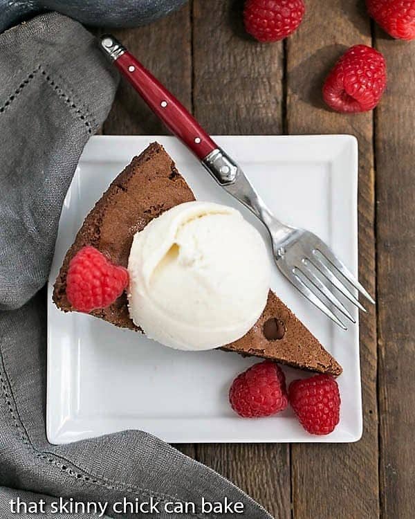 Slice of a Fudgy Skillet Brownies with ice cream and berries on a square white plate with a fork.