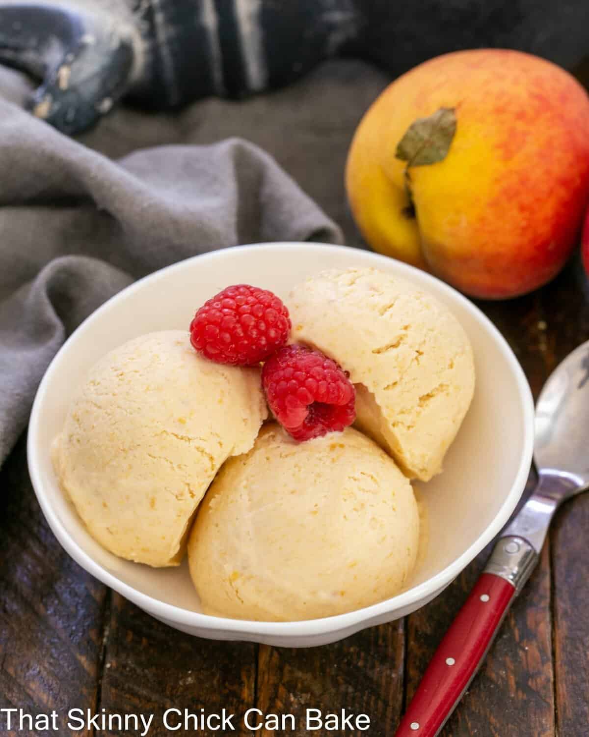 No- Churn Peach ice cream in a shallow bowl with raspberry garnish.