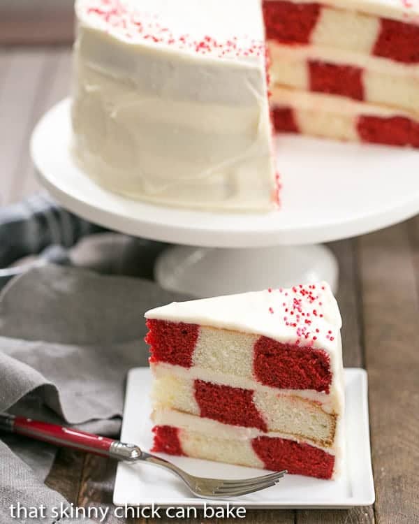 Slice of Red Velvet Checkerboard Cake in front of the whole cake on a cake stand