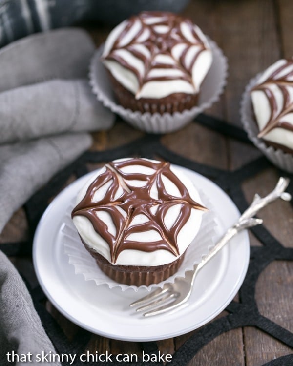 One Spiderweb Cupcake on a white plate with 2 in the background