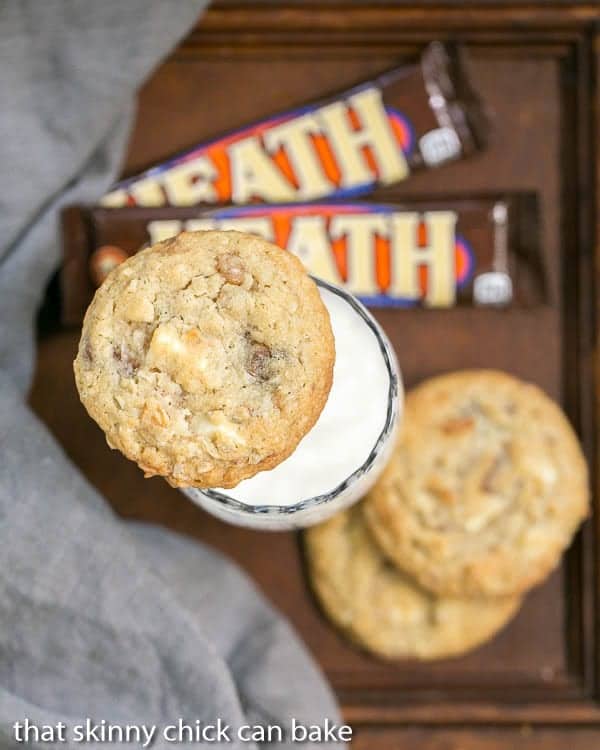 White Chocolate Toffee Chunk Cookies on a glass of milk with Heath bars and a gray napkin