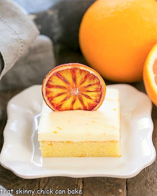 Orange Cake with Cream Cheese Frosting on a square white plate with oranges