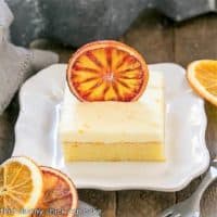 Orange Cake with Cream Cheese Frosting on a square white plate with dried orange slices