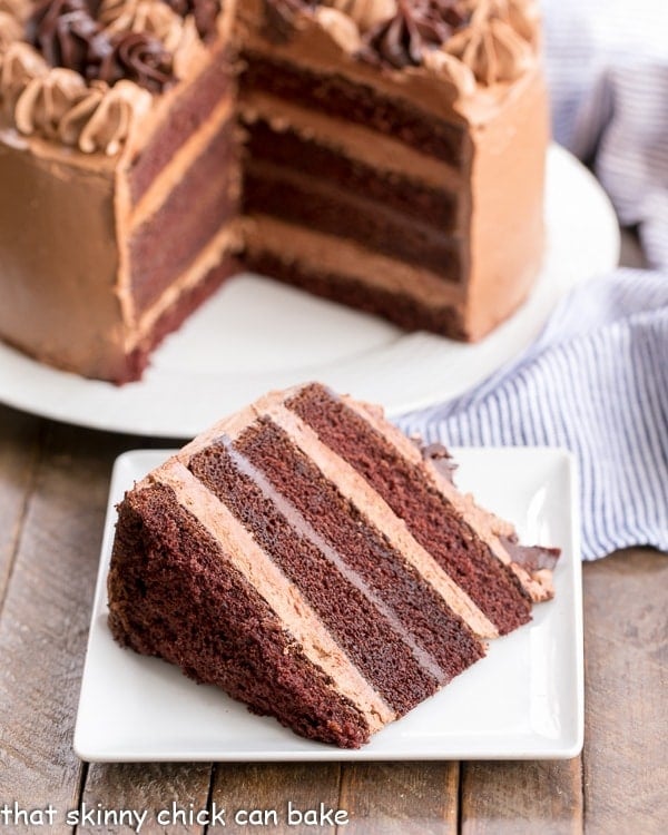 Chocolate Fudge Layer Cake with a slice on a square white plate with cut cake in the background.