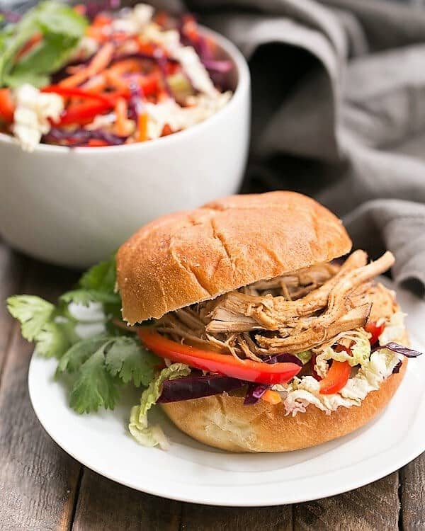 Honey Garlic Chicken Sliders on a white plate with a bowl of slaw