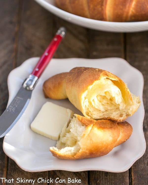 Buttery Homemade Crescent Rolls on a white plate with a red handled knife.