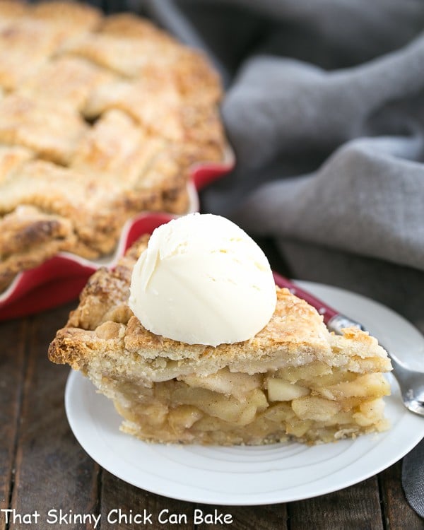 A slice of Deep Dish Apple Pie on a white dessert plate with a scoop of ice cream on top.
