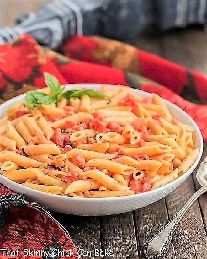 Penne alla Vodka in a white ceramic bowl with a sprig of basil.