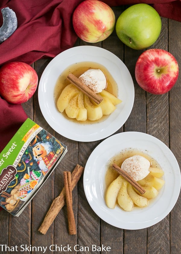 Overhead view of Tea Poached Apples on dessert plates with fresh apples, cinnamon sticks and a box of tea