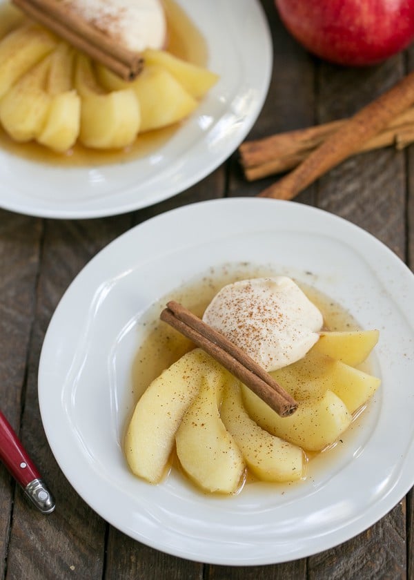 Tea Poached Apples on white plates garnished with cream and cinnamon sticks