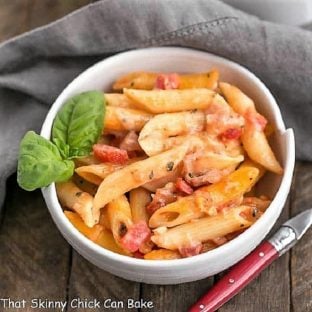 Overhead view of Cheesy Baked Pasta in a white bowl with a sprig of basil