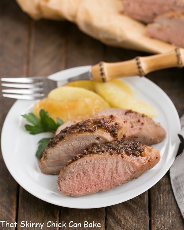 A plate of sliced apple mustard pork tenderloin with a bamboo handle fork.