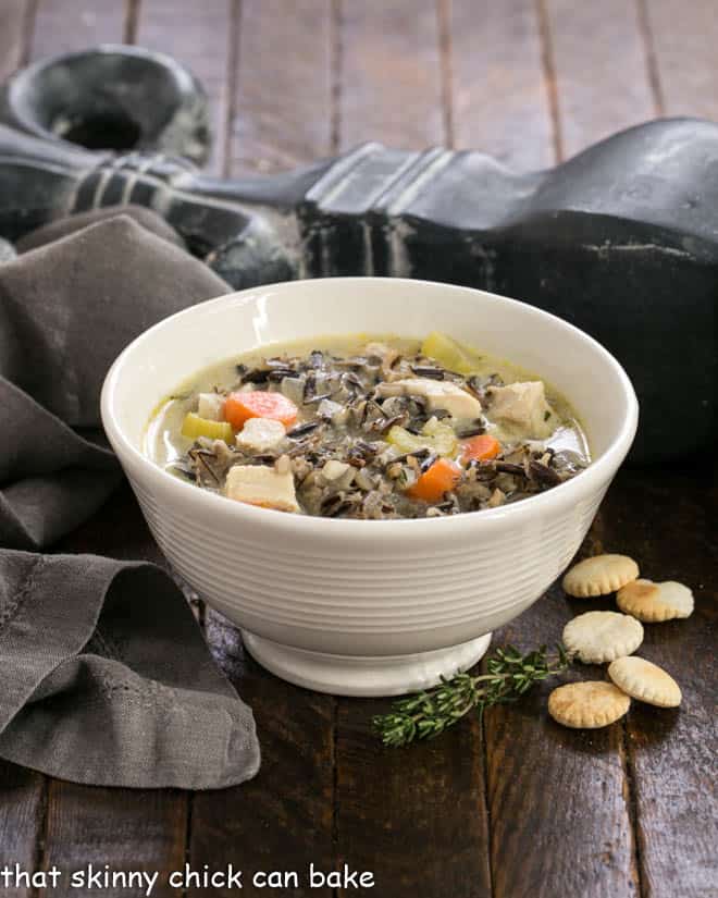 Wild Rice Soup in a white bowl with oyster crackers and a sprig of thyme