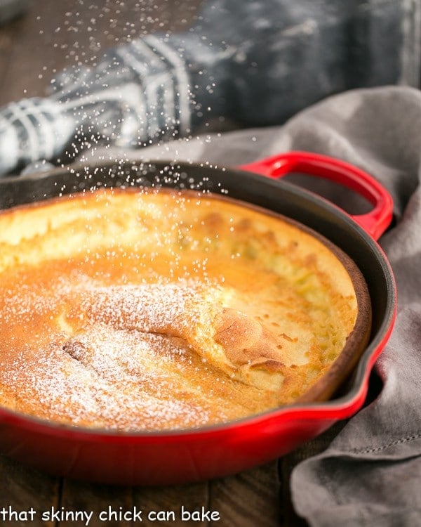 Puffed Pancake - An oven baed pancake topped with berries, whipped cream and powdered sugar! Best Dutch Baby Pancake in a red skillet with a dusting of powdered sugar.