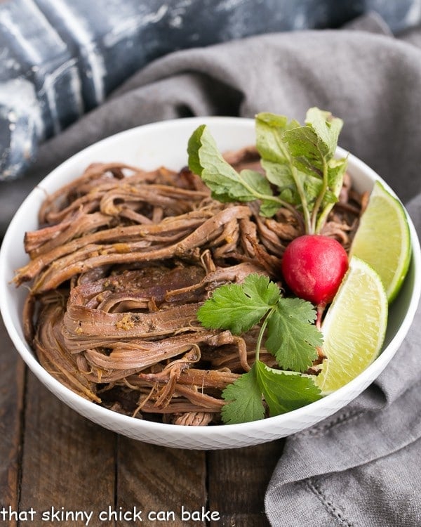 Slow Cooker Carne Asada in a white bowl with a radish and lime wedges