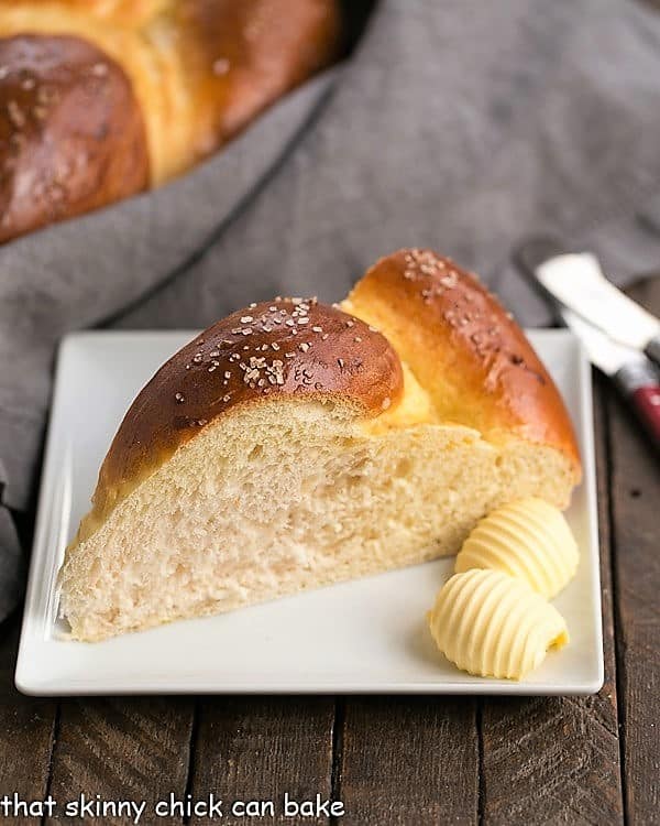 This Braided Easter Bread Recipe is tender, slightly sweet, vanilla scented bread that is perfect to serve at a holiday brunch. This braided Easter bread recipe creates such a tender loaf of homemade egg bread, everyone will scramble for the last piece. #easter #recipe #bread A slice of Braided Easter Bread on a square white plate with 2 pats of butter.