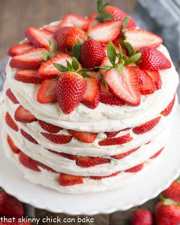 Fresh Strawberry Meringue Cake on a white cake plate. The cake is garnished with a pile of sliced fresh strawberries on top.