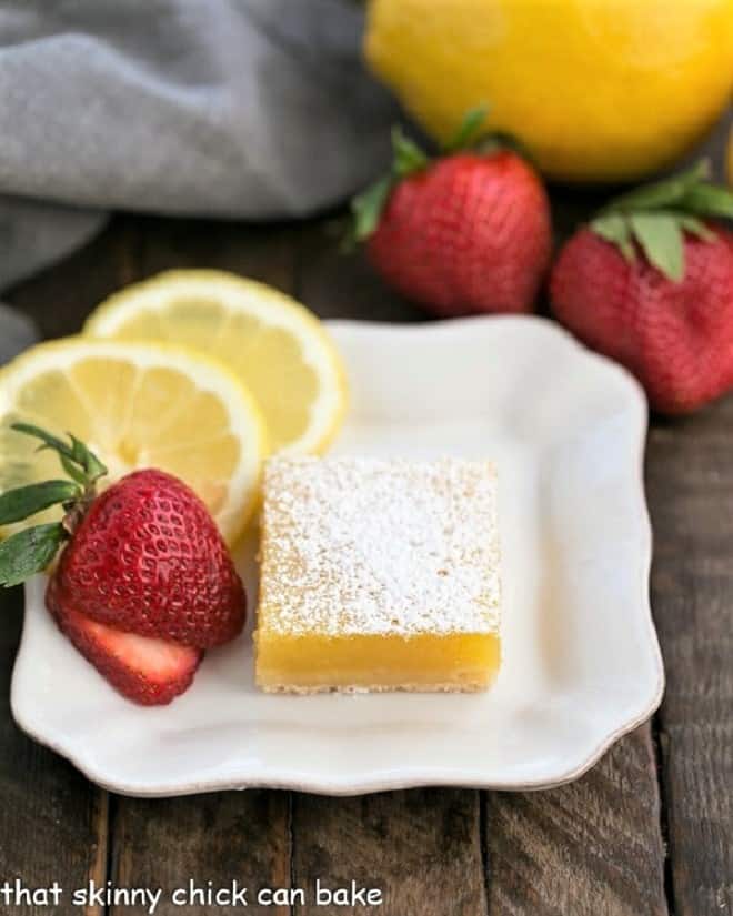 White dessert plate with the Best Lemon Bars, garnished with fresh strawberry slices and slices of lemon.