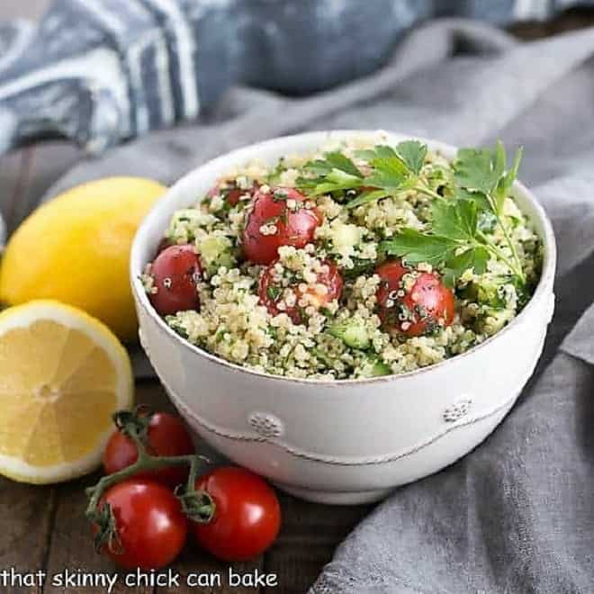 Bowl of quinoa tabbouleh in a white bowl with a lemon and cherry tomatoes.